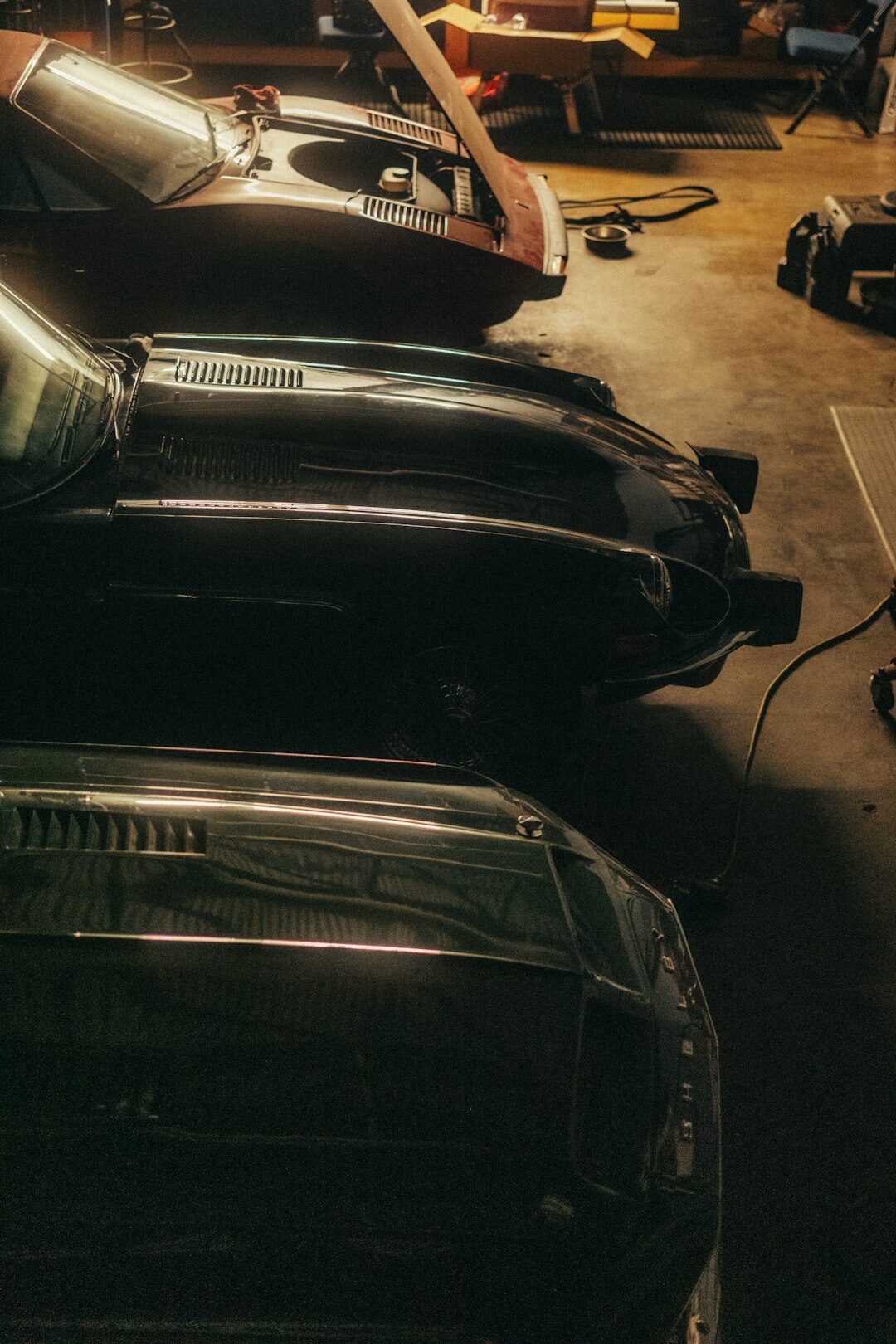 Dimly lit private garage with several classic automobiles covered partially by dust sheets